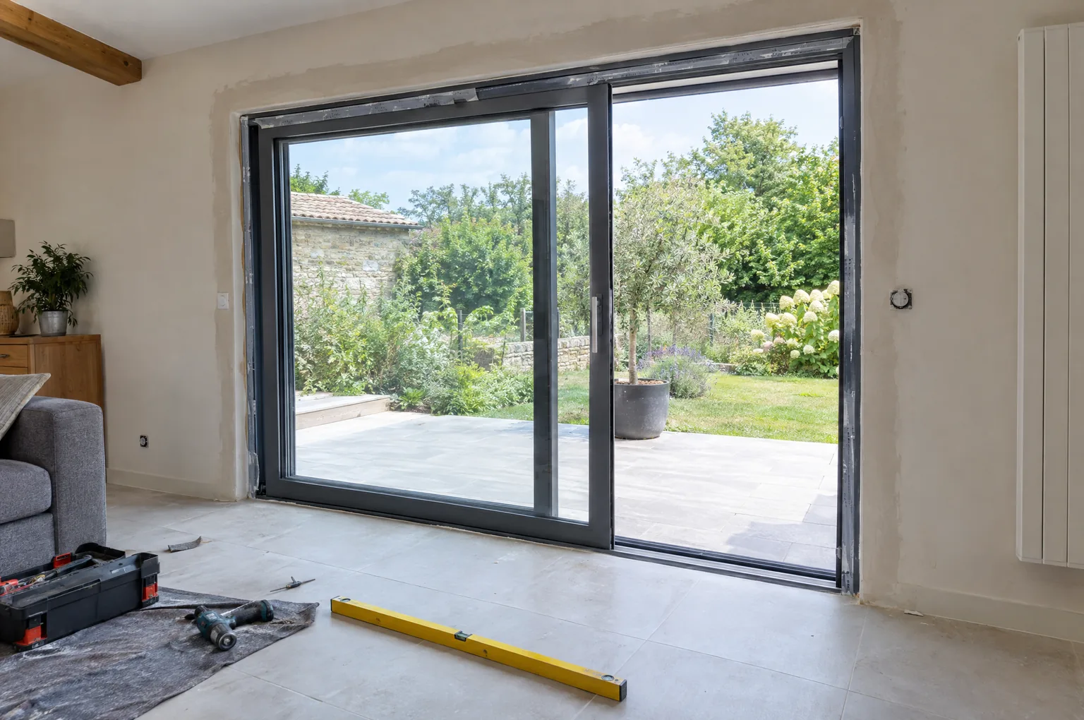 Baie vitrée coulissante en aluminium gris anthracite récemment posée dans un séjour, un vantail entrouvert sur la terrasse