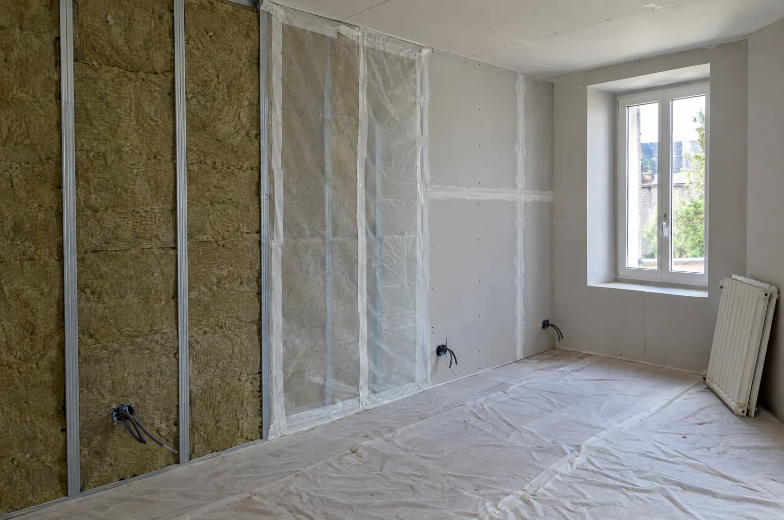 Isolation d’un mur par l’intérieur en cours : ossature métallique garnie de laine minérale, pare-vapeur et plaques de plâtre, radiateur déposé